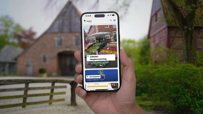 Ein Benutzer präsentiert die neue Webseite der Stadt Vreden auf einem Smartphone im Stadtpark.